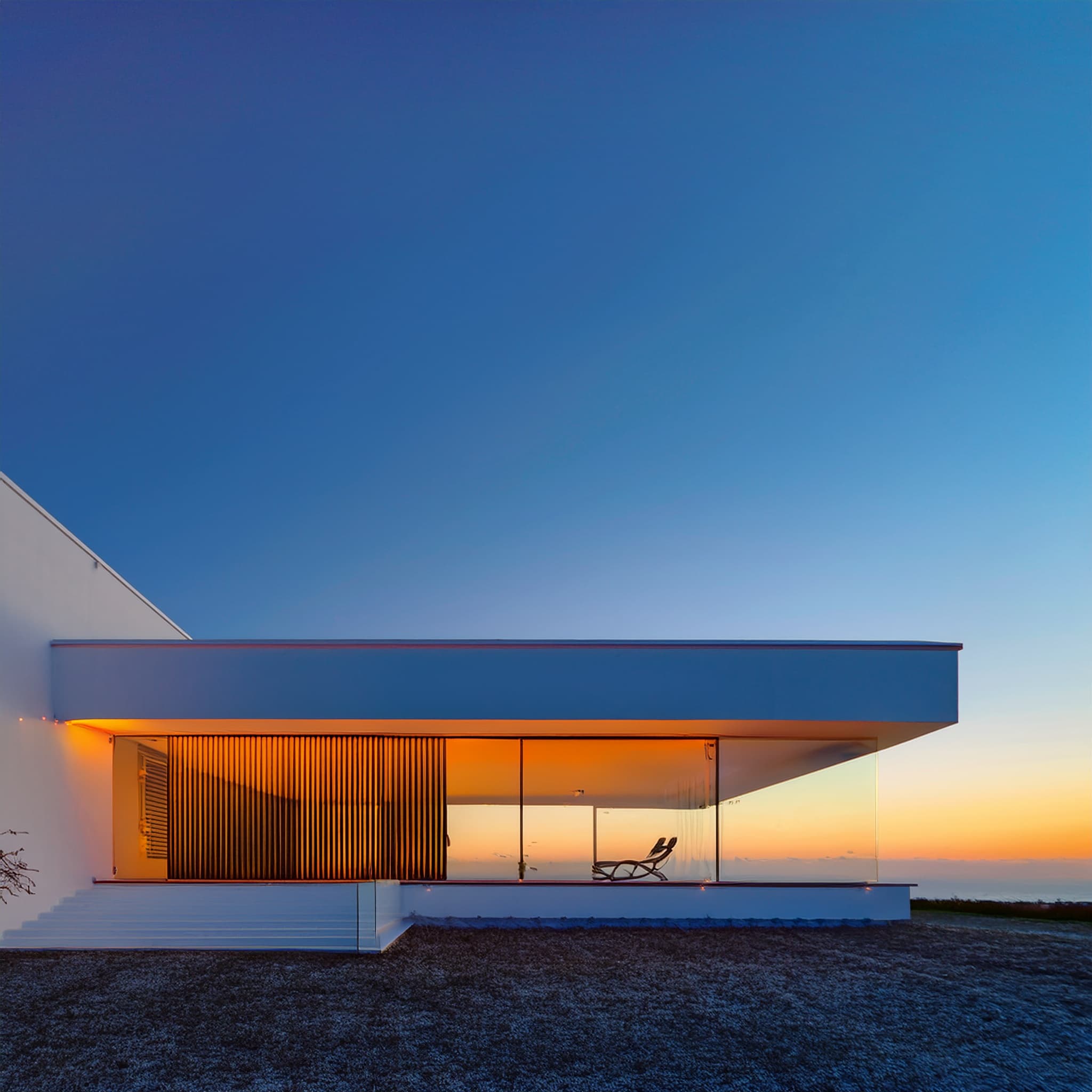 Casa minimalista de cristal frente al mar al atardecer.